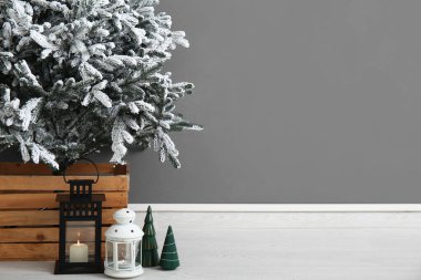 Gri duvarın yanındaki karlı Noel ağacının altında fenerler, yakın plan.