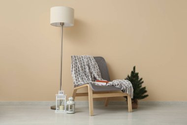 Sıcak battaniyeli rahat koltuk, küçük Noel ağacı ve bej duvarın yanındaki fenerler.