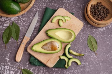Kesik taze avokado ve koyu arkaplanda biberli ahşap tahta.