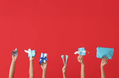 Farklı kozmetik ürünlere ve kırmızı arka planda hediyelere sahip kadın elleri