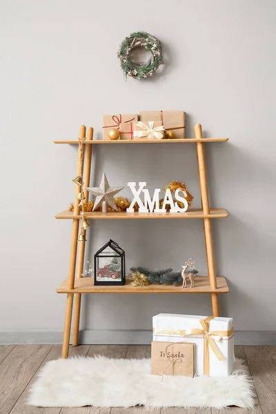 Shelf unit with Christmas decor and presents near light wall in room