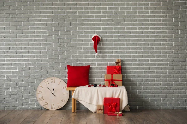 Bench with Christmas presents and clock near grey brick wall in room