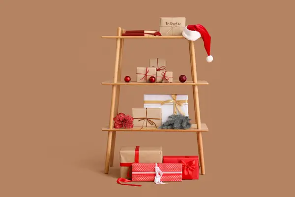 Shelf unit with Christmas presents and decor on brown background
