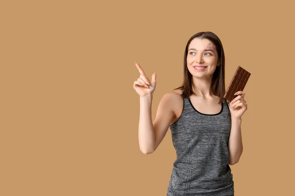 Mladá Žena Drží Čokoládovou Tyčinku Ukazuje Něco Hnědém Pozadí — Stock fotografie