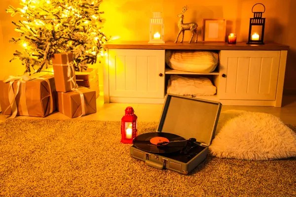 Interior of festive living room with vintage record player and glowing lantern on soft carpet at evening