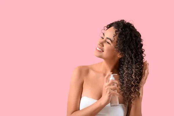 Beautiful African-American woman spraying hair on pink background
