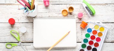 Boş defter, beyaz ahşap arka planda renkli kalemler ve boyalar.