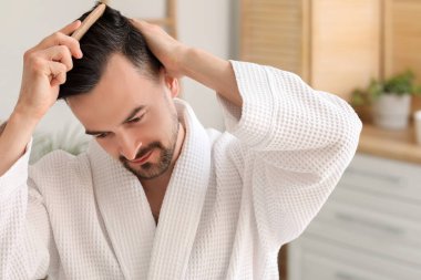 Saç dökülme sorunu olan yakışıklı adam banyoda tarama yapıyor, yakın plan.