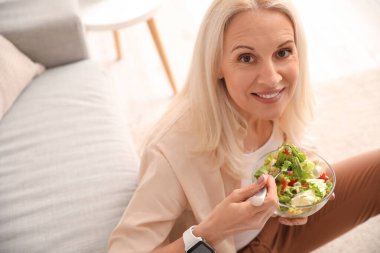 Mature woman eating vegetable salad at home, closeup clipart