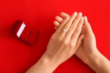 Kırmızı arka planda nişan yüzüğü olan kadın.