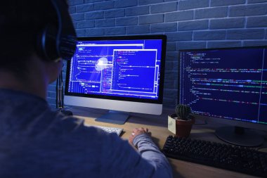 Erkek programcı geceleri ofiste kulaklık ve bilgisayarla çalışıyor.