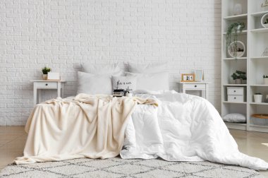 Beyaz battaniyeli dağınık yatak ve hafif yatak odasındaki tepside kahve.