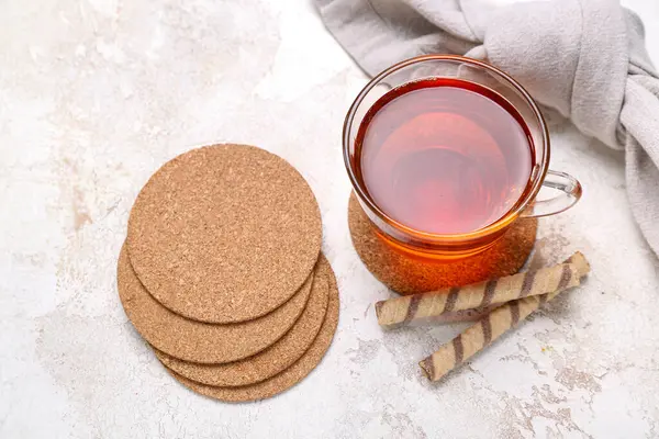 Drink coasters with cup of tea and wafer rolls on white table