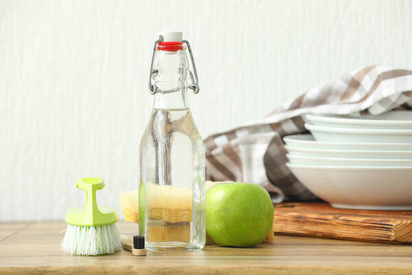 Bottle of vinegar, brushes, sponges and apple on wooden table
