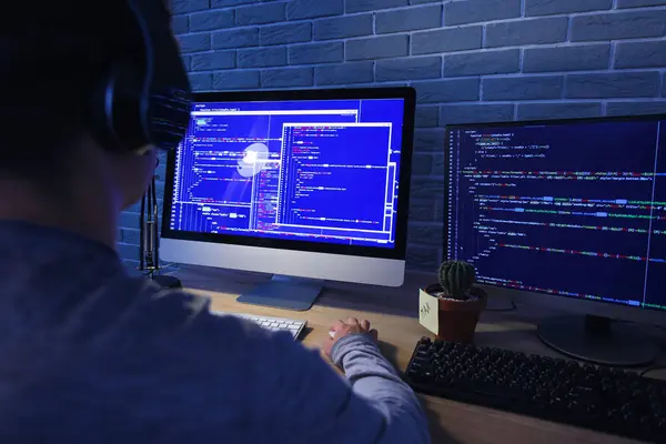 Male programmer working with headphones and computer in office at night