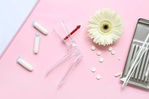 Gynecological speculum, pills, pap smear test tools and menstrual tampons on pink background