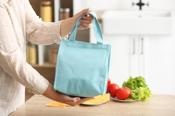 Mother with lunch box bag for school in kitchen