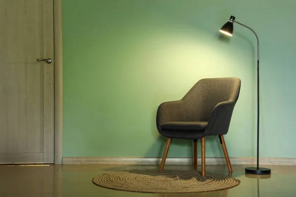 stock image Black armchair with glowing lamp near green wall in room