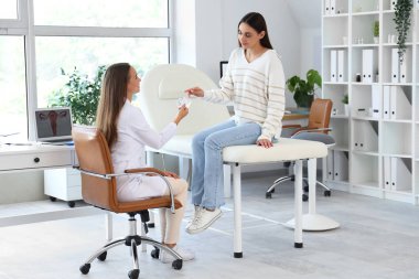 Kadın jinekolog klinikteki hastaya prezervatif veriyor.