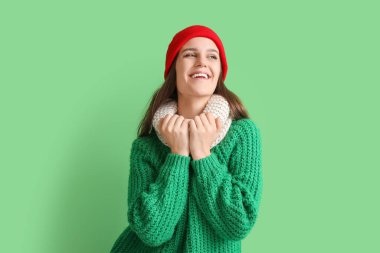 Yeşil arka planda kışın giyinmiş mutlu genç bir kadın.