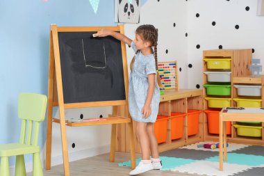 Anaokulunda tahtaya resim çizen küçük kız.