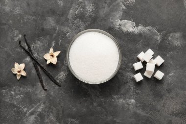 Aromatik vanilya şekerli kase, çiçekler ve siyah arka planda çubuklar