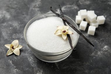 Aromatik vanilya şekerli kase, çiçekler ve siyah arka planda çubuklar