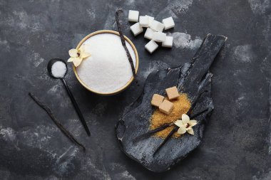 Tahta tahta ve bir kase aromatik vanilya şekeri, siyah arka planda sopaları olan çiçekler.