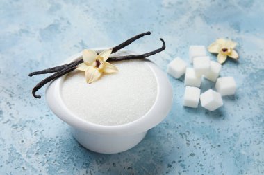 Aromatik vanilya şekerli kase, çiçekler ve mavi arka planda çubuklar