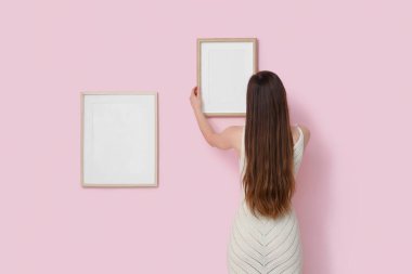 Pembe duvarda boş bir çerçeve asılı genç bir kadın.