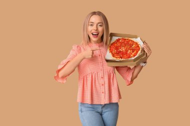 Genç bir kadın kahverengi arka planda lezzetli pizzalar olan karton kutuyu işaret ediyor.