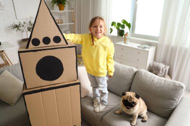 Evde karton roket ve köpek oynayan küçük bir kız.