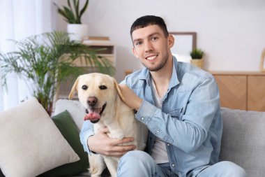 Labrador köpeği olan genç adam evdeki kanepede oturuyor.