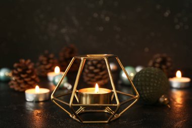 Yanan mumlar, karanlık arka planda Noel topları ve koniler.