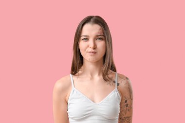 Pembe arka planda yüz geliştirme egzersizi yapan genç bir kadın.