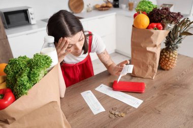 Mutfakta yiyecek ve makbuzları olan üzgün genç bir kadın. Fiyat artışı kavramı