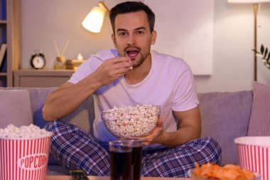 Patlamış mısırlı genç adam akşam evde televizyon izliyor.
