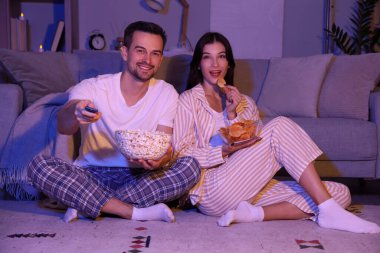 Patates cipsi ve patlamış mısırlı genç çift akşam evde televizyon izliyor.