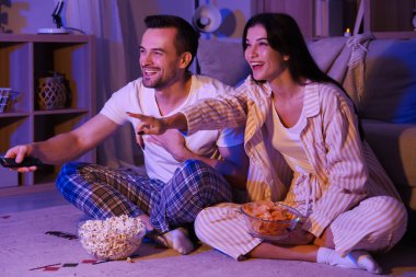 Patates cipsi ve patlamış mısırlı mutlu genç çift akşam evde televizyon izliyor.