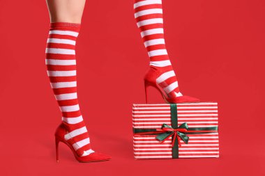 Kırmızı arka planda hediye kutusu olan Noel çoraplı seksi kadın.