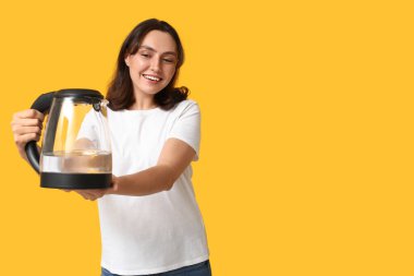 Sarı arka planda modern elektrikli su ısıtıcısı olan güzel genç bir kadın.