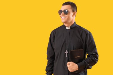 Sarı arka planda kutsal kitabı olan havalı bir rahip.