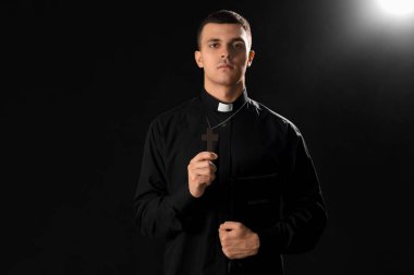 İncil 'i olan genç bir rahip ve karanlık arka planda haç.