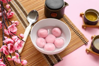 Bambu hasırı, bir kase tangyuan, pembe arka planda çay ve sakura, yakın plan. Dongzhi Festivali