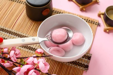 Pembe arka planda bir kase tangyuan ve sakura içeren bambu hasırı, yakın plan. Dongzhi Festivali