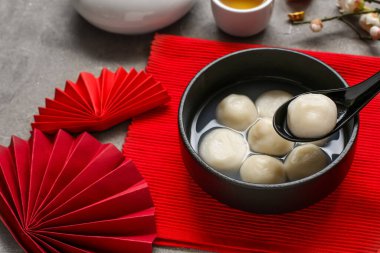 Gri grunge arka planında bir kase tangyuan ve Çin dekoru olan kırmızı hasırlar, yakın plan. Dongzhi Festivali