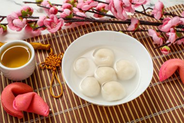 Bambu hasırı, bir kase tangyuan çay, fal kurabiyesi ve beyaz mermer arka planda sakura, yakın plan. Dongzhi Festivali
