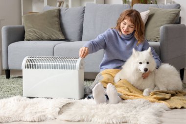 Ekoseli ve Samoylu köpekli genç bir kadın evdeki radyatörün yanında ısınıyor.