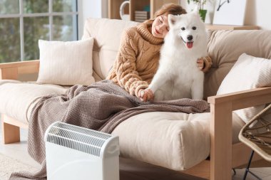 Evdeki radyatörün yanında battaniyeli ve sosisli sandviç ısıtan genç bir kadın.