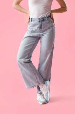 Pembe arka planda açık mavi kotlu genç kadın.